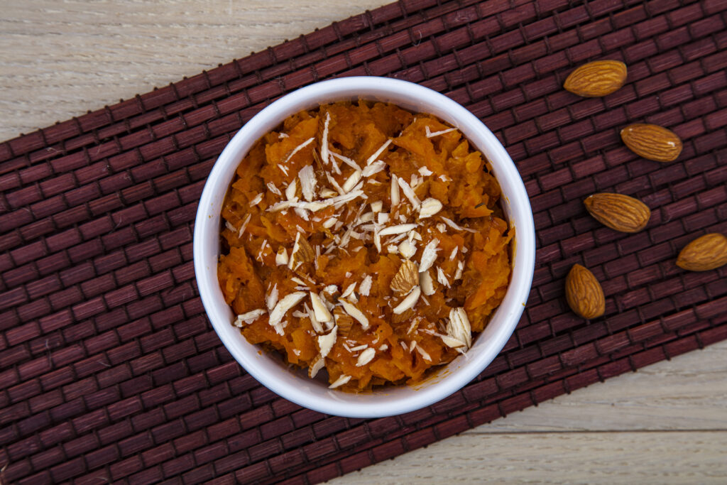 "A bowl of Gajar Ka Halwa garnished with chopped nuts and silver leaf, a traditional Indian carrot dessert, rich in color and texture.