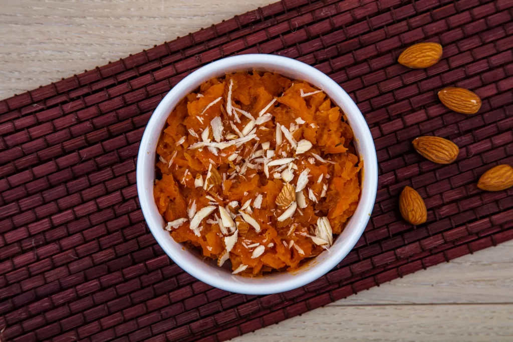 Bowl of gajar ka halwa with almonds on a red placemat.