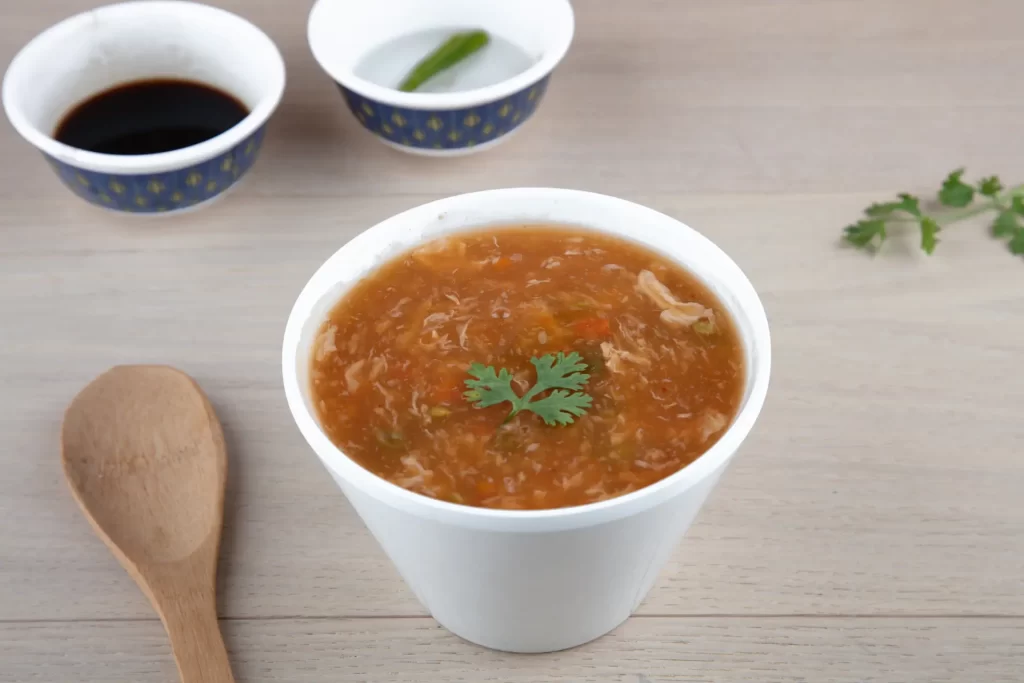 Steaming bowl of hot and sour soup with wooden spoon on table.